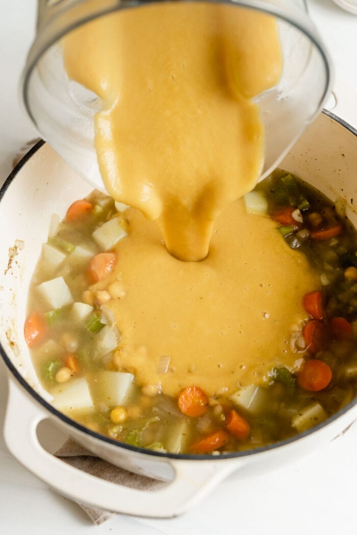 Pouring pureed chickpea soup back into a pot of chunky soup.