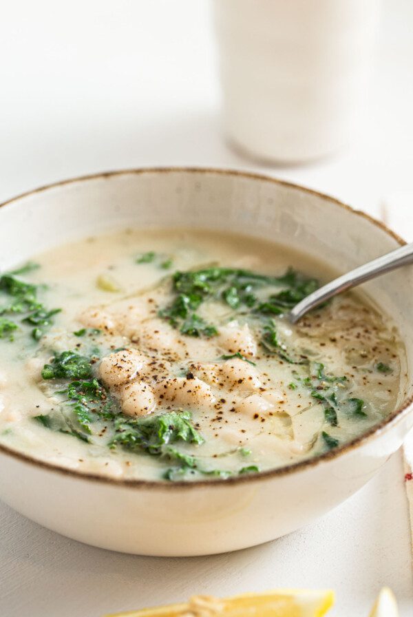 Close up of a bowl of white bean and kale soup topped with fresh-cracked black pepper.
