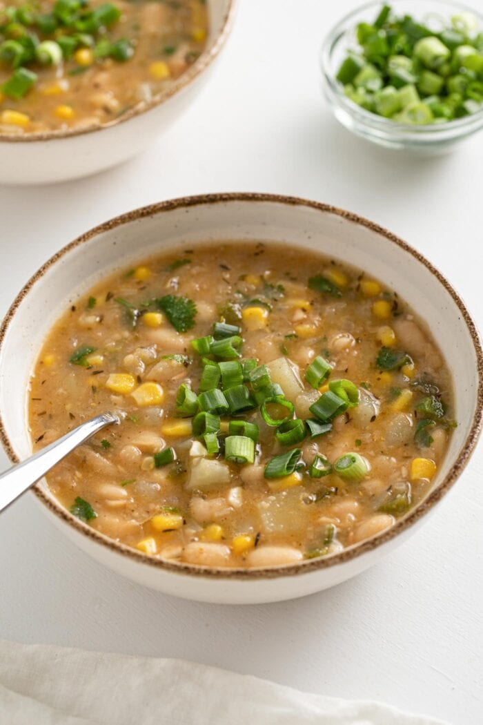 Bowl of white bean and potato chili topped with sliced scallions.
