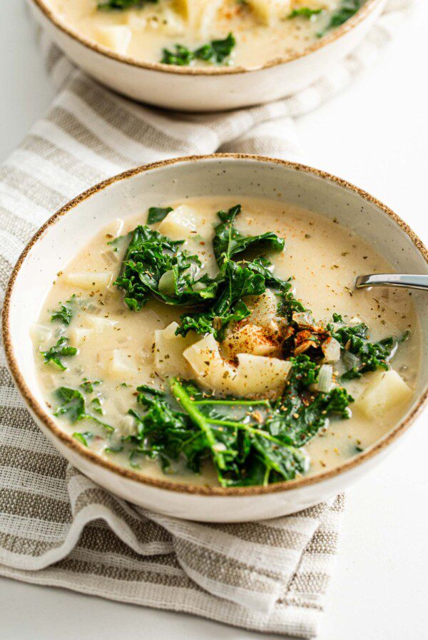 Two bowls of vegan zuppa toscana soup with potato and kale. Spoon rests in bowl.